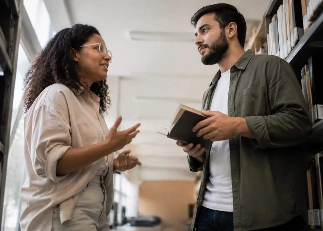 Participantes conversando em pé no corredor entre estantes de livros altas